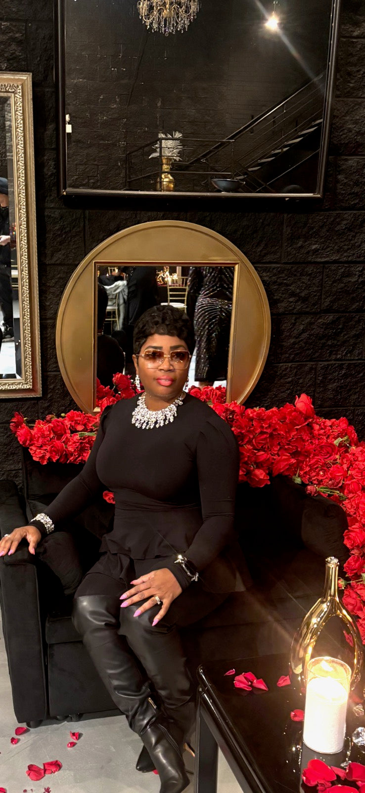 Avanda owner of Pooh Wear Work to Workout sitting on a black couch with red flowers and candles in a stylish room.