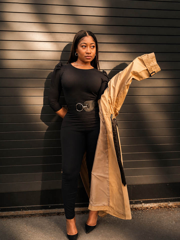 Woman wearing Poohwear holding a beige coat against a black slatted wall